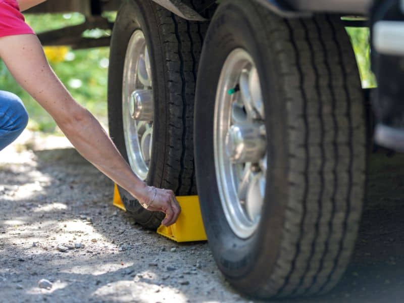 Person placing yellow wheel chocks under a trailer tire - how to jack up a travel trailer