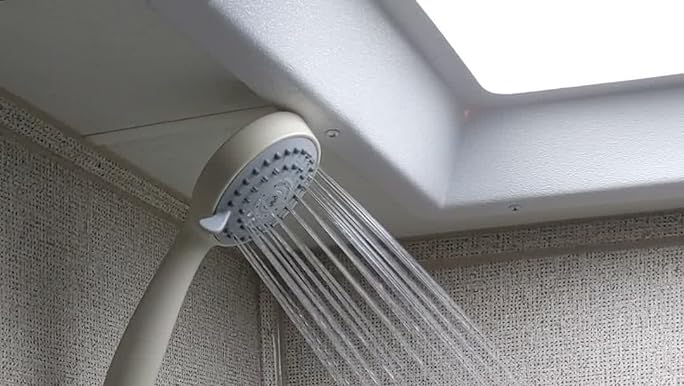 RV showerhead under a roof vent with water sprayinf out into a shower